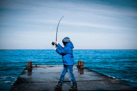 Little boy throws a fishing rod from the pier into the sea. Natural natural compositionの写真素材