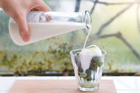 Ice green tea with pouring milk in the glass on the background of nature.の写真素材