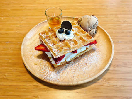 Homemade waffles with blueberry, strawberry, ice cream and honey sauce in plate on wooden table.の写真素材