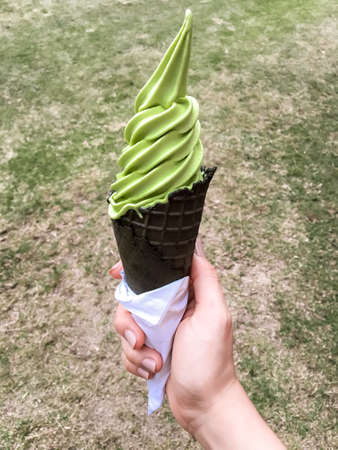 Hand hold ice cream cone green tea with charcoal on grass background.の写真素材