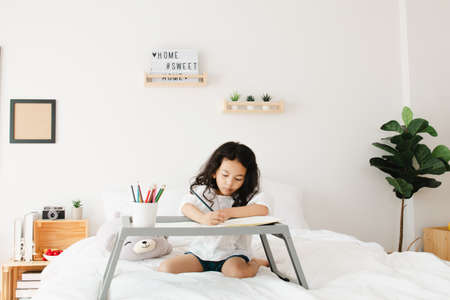 Little kid girl hands detail drawing intently with multicolored pencils in bedroom at home. on white...