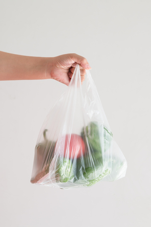 Hand holding a plastic bag of vegetablesの写真素材