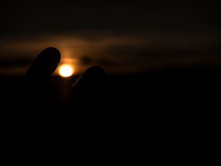 Silhouette of hand holding the sun at sunset, black background