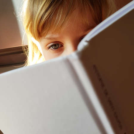 Little blond girl wearing big eye reads a book