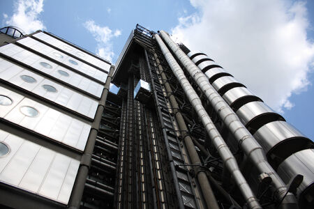 The exterior of a modern office building, showing metal pipes and a lift, against a blue sky with white clouds のeditorial素材