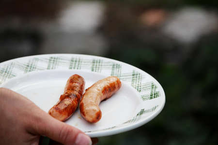 Woman holds white plate with pork sausagesの写真素材