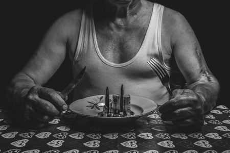 war soldier invalid sitting on the table with fork, knife and plate full of ammunition.Ten-Day War, was initiated by the JNA (Yugoslav People's Army) on 26 June 1991 - 25 June 1991.の写真素材