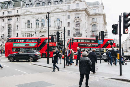 London, UK - 1st April, 2017: Picadilly Circus in London on spring day. Classic red double decker bus passing by, crowded streets, people walking.のeditorial素材