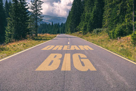 Asphalt road in the mountains going straight up with dream big text message. Conceptual business...