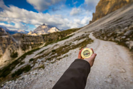 Women hand using a compass in the mountains, travel concept. Hand with compass at mountain road, background of mountains in summer, point of view.の写真素材