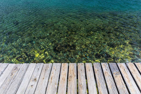 Wooden board empty over sea, can be used for display or present a product. Summer season. Empty perspective wooden planks over the reflection of green water, product display template.の写真素材