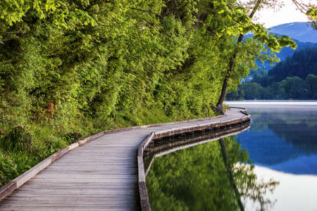 Wooden walkway around the lake Bled with mountains and houses on the background. Beautiful Slovenian...