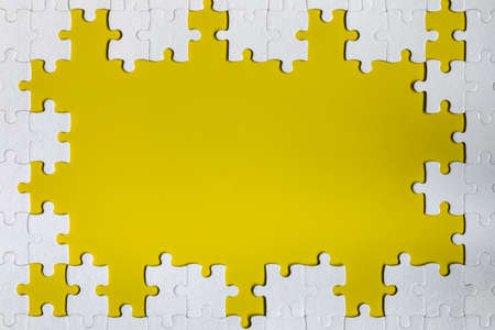 Framing in the form of a rectangle, made of a white jigsaw puzzle. Frame text and jigsaw puzzles. Frame made of jigsaw puzzle pieces on yellow background.の写真素材