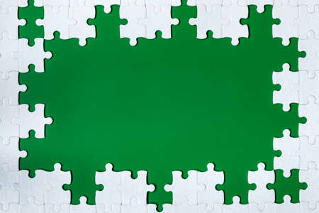 Framing in the form of a rectangle, made of a white jigsaw puzzle. Frame text and jigsaw puzzles. Frame made of jigsaw puzzle pieces on green background.の写真素材