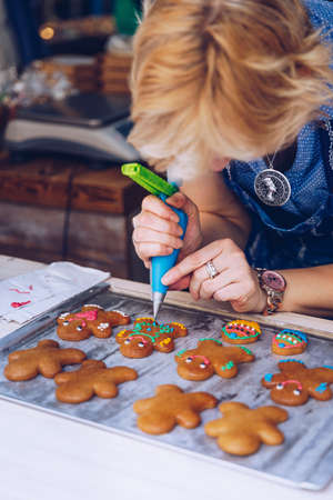 Unrecognizable women confectioner hand decorating a gingerman with a pastry bag, drawing a smile, making it cute, fun and delicious. Woman making ginger bread cookies in the kitchen.の写真素材