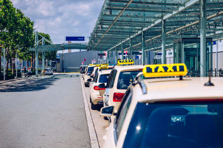 Taxi cabs waiting for passengers. Yellow taxi sign on cab cars. Taxi cars waiting arrival passengers in front of Airport Gate. Taxis stand on Airport Terminal waiting for passengers.の写真素材
