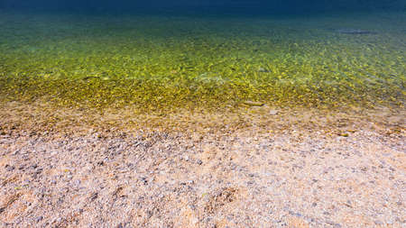 Stones under water. Sea pebbles on the beach. Sea pebbles on the beach sand with transparent water. Natural sea stones closeup. Beach smooth pebbles. Tourism and travel themed. Vacation background.の写真素材
