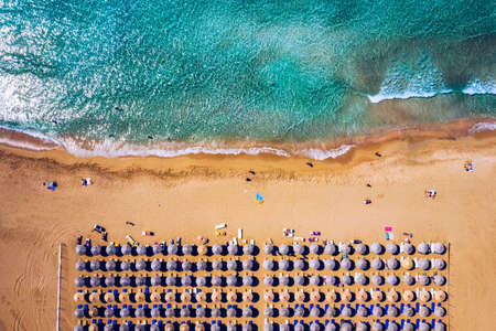 Aerial view of sandy beach with colorful umbrellas, swimming people in sea bay with transparent blue water at sunset in summer. Aerial top view on the beach, umbrellas, sand and sea waves.の写真素材