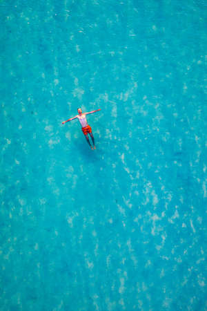 Drone view of a man floating in tropical sea water. Aerial view of young man floating on sea water enjoying sunbathing and vacations in tropical destination. People travel tourism holidays concept. の写真素材