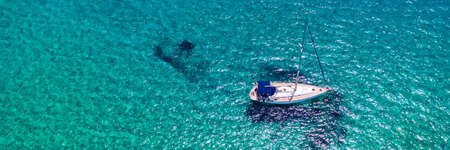 Yacht anchoring in crystal clear turquoise water in front of the tropical island, alternative lifestyle, living on a boat. Aerial view of yacht at anchor on turquoise water, showing luxury, wealth.の写真素材