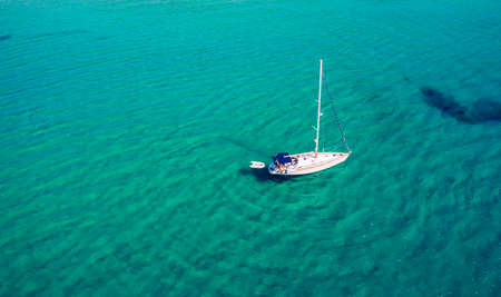 Aerial view of anchored sailing yacht in emerald sea. Aerial view of a boat. Outdoor water sports,...