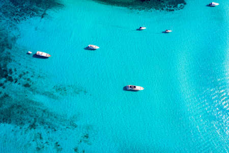 Yacht anchoring in crystal clear turquoise water in front of the tropical island, alternative lifestyle, living on a boat. Aerial view of yacht at anchor on turquoise water, showing luxury, wealth.の写真素材