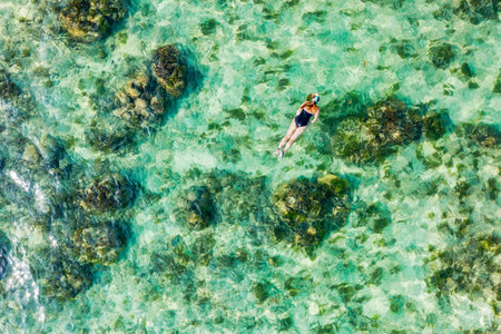 Aerial view of unrecognizable women snorkelling in tropical waters. Aerial view around a young women snorkeling above coral reef reaching deeper parts of the crystal clear water, Mauritius.の写真素材