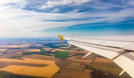 Airplane windows view above the earth on landmark down. View from an airplane window over a wing flying high above farmlands and fields. View from window of plane airplane flying.の写真素材