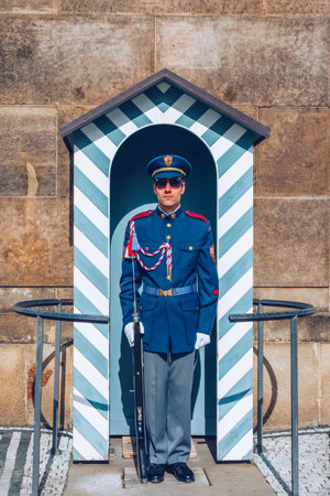 Prague, Czechia - April 11, 2024: A solitary guard stands at attention in a striped sentry box at Prague Castle during a sunny afternoon at a historic site.の写真素材