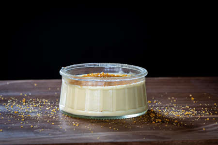 Dish of Creme BrÃ»lÃ©e french dessert sprinkled with sugar in a glass bowl on a wood surfaceの写真素材