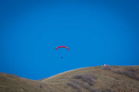 Paraglider with a red and yellow parachute wing peacefully gliding through a blue skyの写真素材
