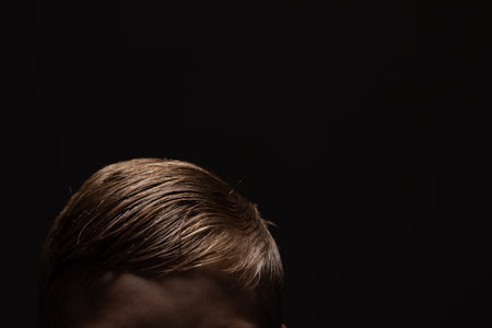 The top of a boys head with a black background