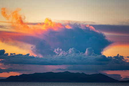Puffy orange and blue clouds hovering over an island
