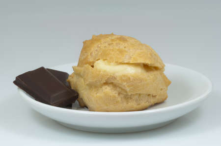 single cream puff with pieces of chocolate on the coffee-cup plate and white background - DSC0700の写真素材