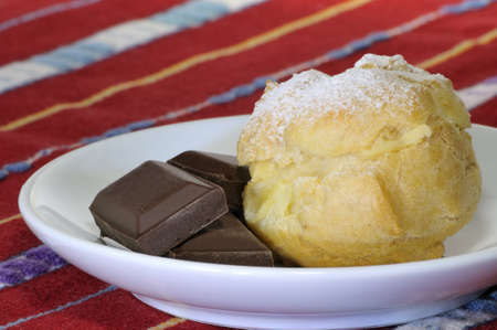 single cream puff with sugar and pieces of chocolate on the coffee-cup plate and red cloth background - DSC0864の写真素材