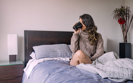 Latin woman lying in her bedroom having a cup of coffee in the morningの写真素材