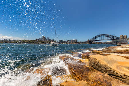 View of Harbor Bridge with a boat sailing in the distance and water splashing in the foreground in Sydney, Australiaの写真素材