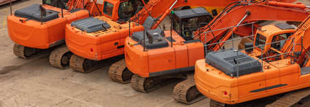 Old orange heavy excavators parked in one row on concrete surface. Construction site. Aerial angled...