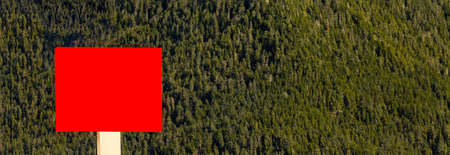 Blank red sign in the foreground and forest, mountains, blue sky with clouds in the background