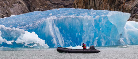 Single tourist sailing in a speed boat by a huge iceberg floating in a fjord. Alaska, USA