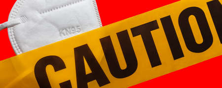 Facial protective mask KN95 covered by yellow caution tape. Isolated. Red background. Protection against viruses, bacteria, germs. PPE. Quarantine.の写真素材