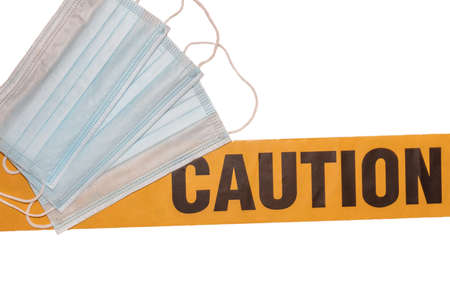 Facial protective masks on top of yellow caution tape. Isolated. White background. Protection against viruses and bacteria. PPE. Quarantine area.の写真素材