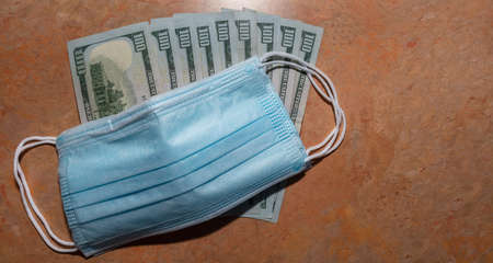 Facial protective surgical masks on top of a few hundred dollar bills. Marble table background. Expensive protection against viruses and bacteria.の写真素材