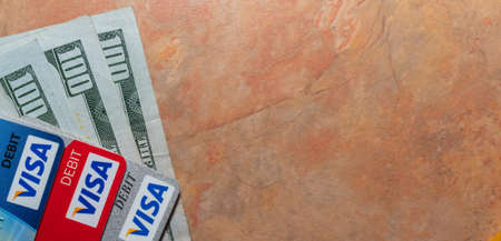 Miami, Florida - May 29, 2020: Hundred dollar bills and visa debit cards on top of them. Marble...