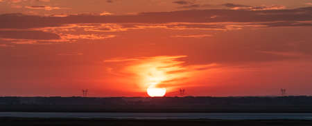 Beautiful panoramic landscape at sunset. Red and orange sky. High voltage power lines in the distance next to the Sun disk. Russian country side in Altai Krai, Siberia.の写真素材