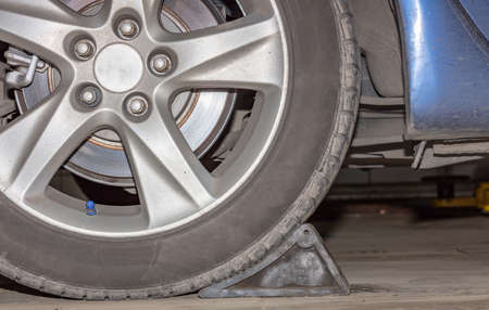 Car wheel on a car with a wheel stopper, close-up, wheel tuning disk and tire in repair workshop.