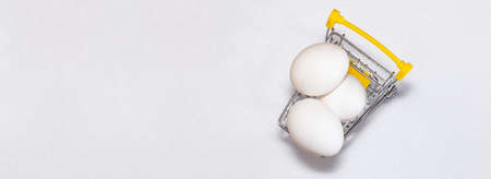Fresh eggs in a shopping cart. Top view. Shopping, purchasing, and food delivery concept. White background. Close up shot. Isolated. Panorama, banner size with copy space.の写真素材