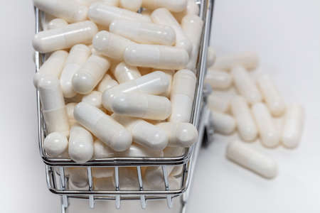 High angle shot of a small shopping cart full of white pills. White background. Close up shot. Some pills under the cart blurry in the background. Shopping online, pharmaceutical business concepts.の写真素材