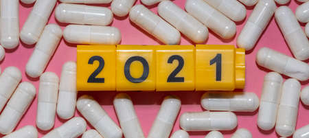 Top close up shot of white pills surrounding yellow cubes with black digits which form 2021 year....