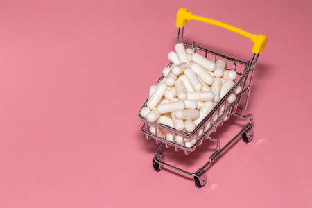 High angle shot of a small shopping cart full of white pills. Pink background, copy space. Shopping online, buying medicine, pharmaceutical business concepts.の写真素材
